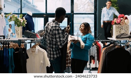 Cheerful couple playing with stylish merchandise, fooling with trendy clothes in modern boutique. African american customers shopping for fashionable items for new wardrobe. Fashion concept