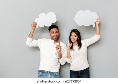 Cheerful couple pointing their fingers up and holding empty bubbles isolated