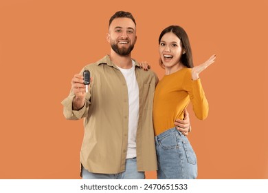 A cheerful couple is seen holding a set of car keys against a vibrant orange backdrop. The man displays the keys while the woman makes an enthusiastic gesture, indicating their joy and excitement - Powered by Shutterstock