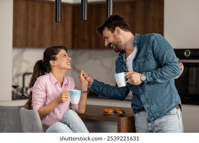 A cheerful couple shares a moment of laughter over morning coffee in a modern kitchen, displaying warmth and connection. Relaxation and happiness are evident in their engaging conversation. - Powered by Shutterstock