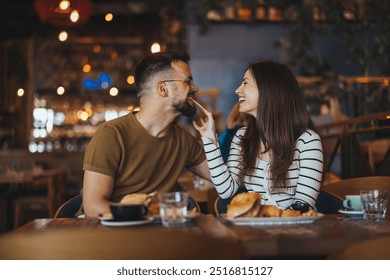 Cheerful couple sharing a joyful moment while having breakfast in a cozy cafe setting, demonstrating love and happiness. - Powered by Shutterstock