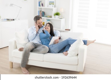 cheerful couple sharing music on digital tablet in sofa at home