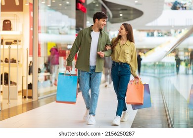 Cheerful Couple Shopping Walking Holding Hands Carrying Colorful Shopper Bags Enjoying Weekend In Mall Indoor. Seasonal Sales Offer, Consumerism Concept. Full Length Shot - Powered by Shutterstock