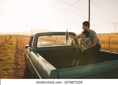 Cheerful couple sitting in the back of their pickup truck enjoying the road trip in country side. Couple taking a selfie using mobile phone sitting at the back of their pick up truck. - Powered by Shutterstock