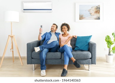 Cheerful couple sitting on sofa switching on air conditioner