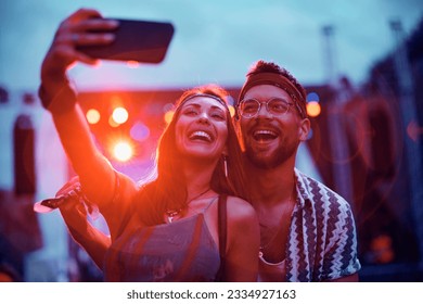 Cheerful couple taking selfie in front of a stage during summer music concert. - Powered by Shutterstock