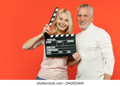 Cheerful Couple Two Friends Elderly Gray-haired Man Blonde Woman In White Pink Casual Clothes Hold Classic Black Film Making Clapperboard Isolated On Bright Orange Color Background Studio Portrait