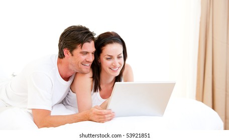 Cheerful couple using a computer lying on their bed at home - Powered by Shutterstock