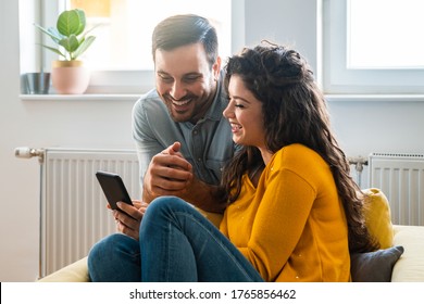 Cheerful Couple Using Mobile Phone At Home Stock Photo