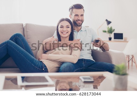 Cheerful couple is watching tv together and having fun. They are in the living room of their apartment