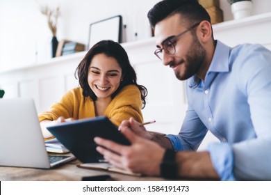 Cheerful couple wearing casual clothes writing notes in notebook while using laptop and tablet and sitting at table at home - Powered by Shutterstock