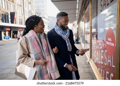 Cheerful Couple Window Shopping In Town With Mobile, Looking Through Store Window