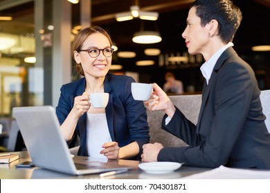 Cheerful coworkers in formalwear chatting animatedly with each other while enjoying fragrant coffee at cozy cafe