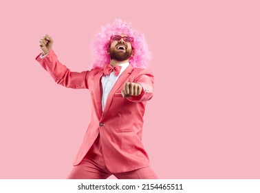 Cheerful Crazy Man In Pink Wig Making Funny Dance Moves Isolated On Pink Background. Eccentric Man In Pink Formal Suit Rejoices, Has Fun And Dances In Gangnam Style. Banner.