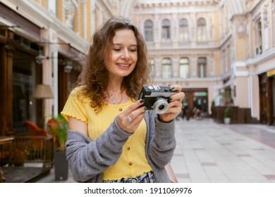 Cheerful curly hair woman tourist with retro camera in city. Travel concept