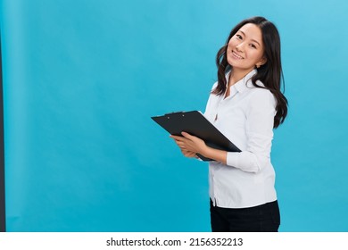 Cheerful Cute Asian Businesswoman In Classic Office Dress Code Holds Folder Tablet With Successful Test Results Posing Isolated On Blue Studio Background. Cool Business Offer. Job Interview Concept