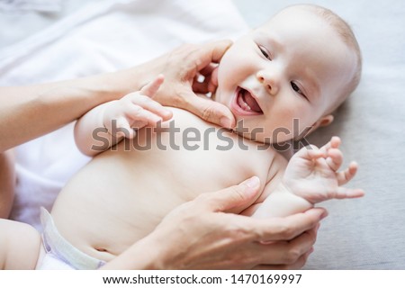 Cheerful cute baby girl lying on bed while mother looking at her first teeth