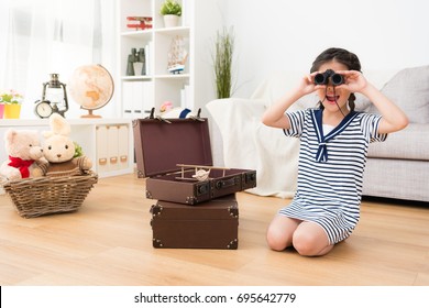 cheerful cute female kid sailor playing adventure game with toy in living room and using telescope tool searching goal feeling happy.