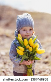 A Cheerful Cute Little Boy With Red Hair Holding Yellow Tulips Having Fun Outside In Early Spring In The Forest Near The Water.