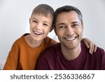 Cheerful cute son kid and happy Latin dad posing for family portrait together, sitting close, hugging, looking at camera, smiling, laughing. Positive child and father head shot with white background