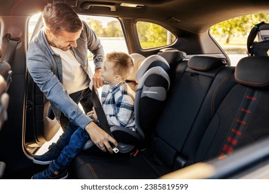 A cheerful dad is buckling up his son in his car seat and preparing for trip. - Powered by Shutterstock