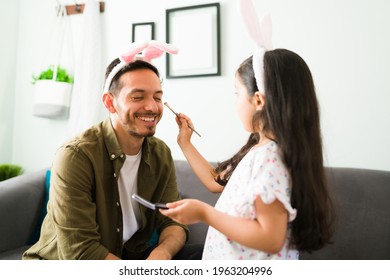 Cheerful Dad With Bunny Ears Playing With Her Little Daughter. Beautiful Girl Putting Makeup And Eyeshadow To Her Father