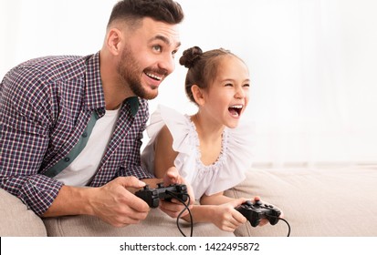 Cheerful Dad Enjoying Video Game With His Cute Daughter, Playing With Joysticks At Home, Empty Space