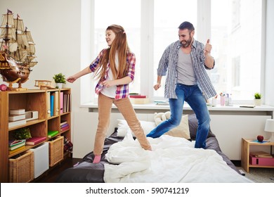 Cheerful Dad Helping His Little Daughter To Rehearse Dance Before School Concert, They Standing On Bed Against Panoramic Window