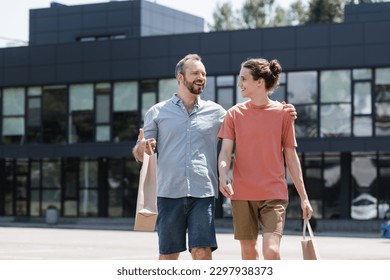 cheerful dad hugging happy teenage son while walking from mall with shopping bags - Powered by Shutterstock