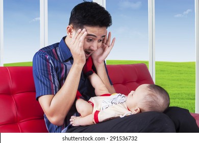 Cheerful Dad Sitting On Sofa While Playing Peekaboo With His Baby, Shot At Home