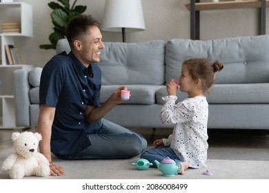 Cheerful daddy and sweet happy preschool daughter kid playing tea party, pretending drinking coffee, tea from toy cups, using plastic dish, enjoying game, playtime, family leisure time - Shutterstock ID 2086008499
