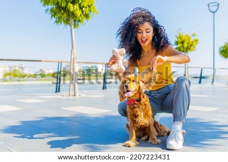 Cheerful dark long curly haired woman with american cocker dog playing in summer park