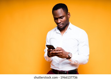 Cheerful dark-skinned office worker stands on a yellow background and works on the phone