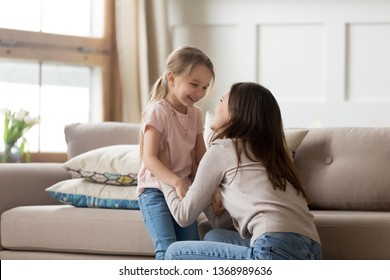 Cheerful Daughter Looking At Overjoyed Mother Laughing Having Fun In Living Room At Home, Older Younger Sister Enjoy Time Together Spend Funny Activity On Weekend, Love And Care Tender Moment Concept