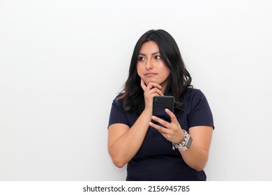 Cheerful delighted latin woman types and receive messages on modern cell phone device, enjoys good internet connection, dressed in black t-shirt, focused aside, isolated on white wall 