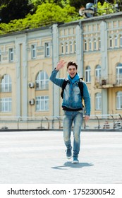 Cheerful Delivery Man With Backpack Waving Hand On City Street