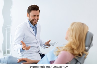 Cheerful Dentist Handsome Millennial Man In Workwear Having Conversation With Blonde Woman Patient Sitting At Dental Chair, Smiling And Gesturing, Side View. Doctor And Patient Relationship