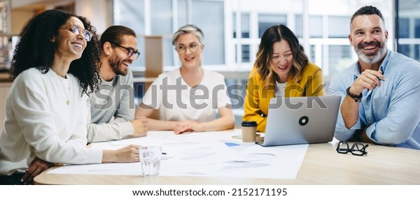 Cheerful design\
professionals smiling happily during a meeting in a modern office.\
Group of innovative businesspeople sharing creative ideas while\
working on a new\
project.