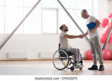 Cheerful Disabled Patient Greeting His Physical Therapist In The Gym