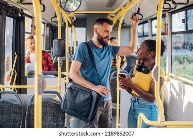 Cheerful diverse friends smiling and talking together and using a smartphone while riding a bus in the city and going to work. Standing in public transport, commuting by bus. Diverse romantic couple. - Powered by Shutterstock