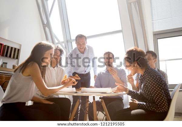 Cheerful diverse team people workers students\
laughing at funny joke while eating pizza together, friendly\
multi-ethnic colleagues group talking enjoying having fun and\
corporate lunch in office\
room