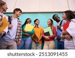 Cheerful diverse university students meeting looking smiling each other standing outdoors. Young international people in community of friends with backpacks and workbooks in front blue wall background