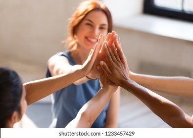 Cheerful diverse young girls sitting together in sports studio before starts training giving high five feel happy and healthy, close up focus on hands. Respect and trust, celebration and amity concept