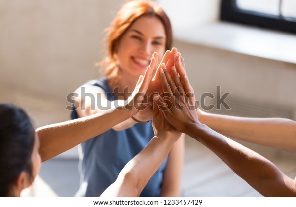 Cheerful diverse young girls sitting together in\
sports studio before starts training giving high five feel happy\
and healthy, close up focus on hands. Respect and trust,\
celebration and amity\
concept