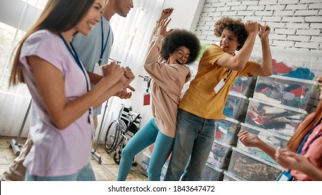 Cheerful diverse young volunteers dancing, having fun while celebrating success in charitable organization office, Selective focus, Web Banner - Powered by Shutterstock