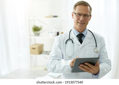 Cheerful Doctor In Lab Coat Using Tablet Computer In Clinic