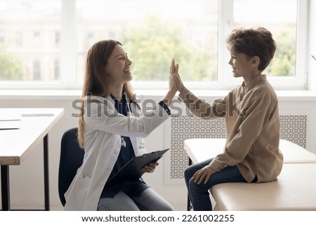 Cheerful doctor and patient kid giving high five in clinic office, laughing after successful examination. Happy pediatrician clapping greeting hands with healthy child, laughing