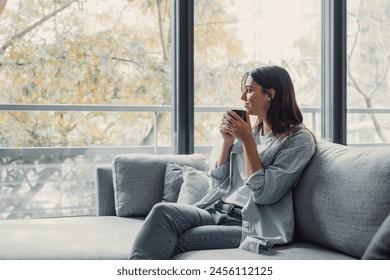 Cheerful dreamy girl holding mug of hot beverage, looking away in deep good thoughts, smiling, dreaming, enjoying aromatic herbal tea, smelling morning coffee, warming hands - Powered by Shutterstock