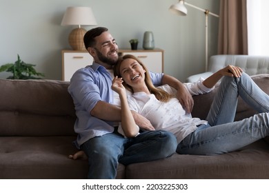 Cheerful dreamy married couple enjoying leisure on sofa, hugging, talking, chatting, laughing, dreaming, thinking over family plans, discussing real estate buying. - Powered by Shutterstock