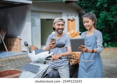 A cheerful duo engages with digital devices next to a scooter loaded with delivery goods